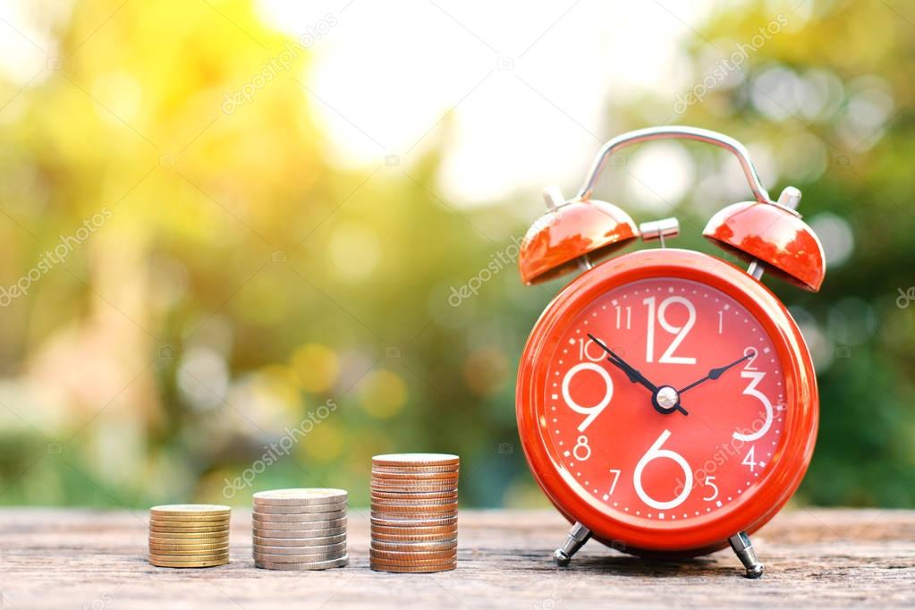 Red alarm clock with coin on old wood tree