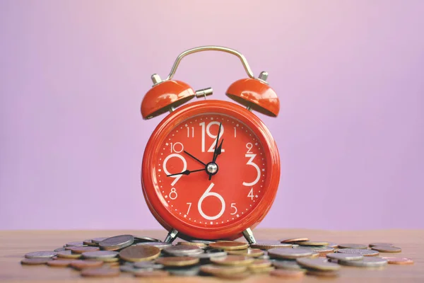 Reloj despertador rojo y moneda sobre tabla de madera fondo púrpura — Foto de Stock
