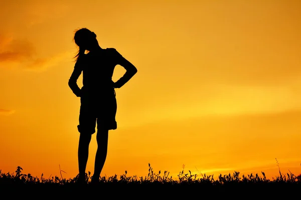 Silhouette di ragazza felice in piedi sul campo di erba e cielo tramonto — Foto Stock
