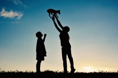 Siluet anne ve çocuk küçük köpekle oynamayı 