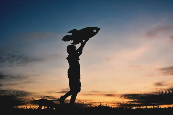 Silhouette garçon tenant un papier fusée et jouant avec petit chien — Photo