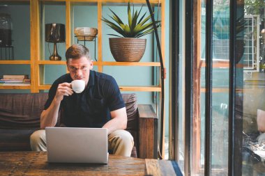 Mutlu yakışıklı genç adam bilgisayar kullanarak ile kahve içme