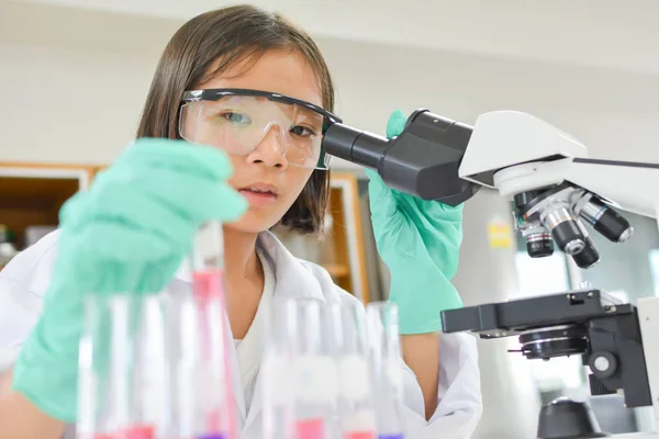Menina segurando tubo de ensaio e usando microscópio — Fotografia de Stock