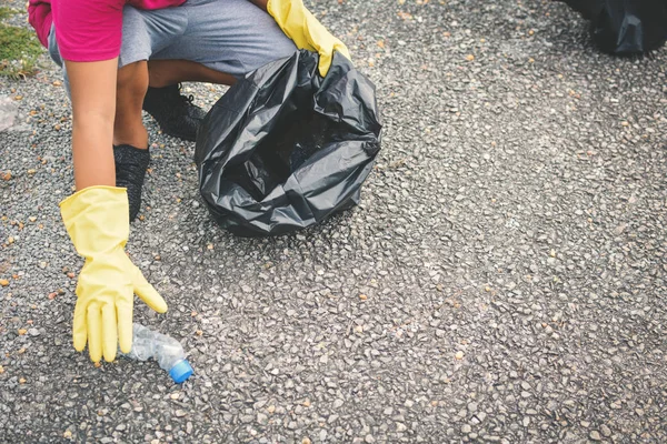 Ręka chłopca w rękawice żółty, zbierając puste butelki plastikowe do worka bin — Zdjęcie stockowe