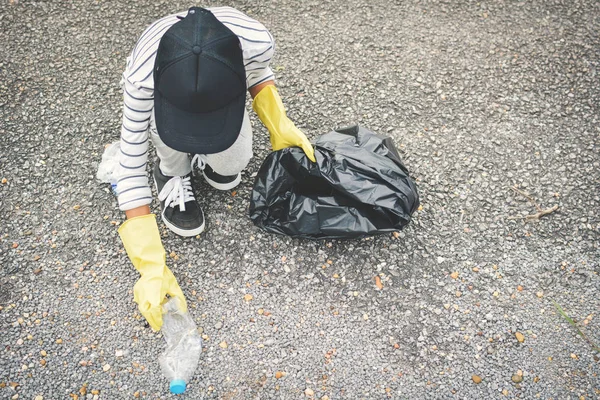 Ręka dziewczyna w rękawice żółty, zbierając puste butelki plastikowe do worka bin — Zdjęcie stockowe