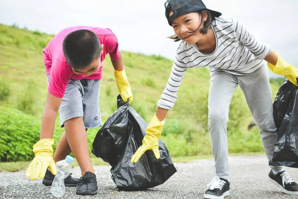 Los niños entregan guantes amarillos recogiendo el plástico vacío de la botella en la bolsa de basura —  Fotos de Stock