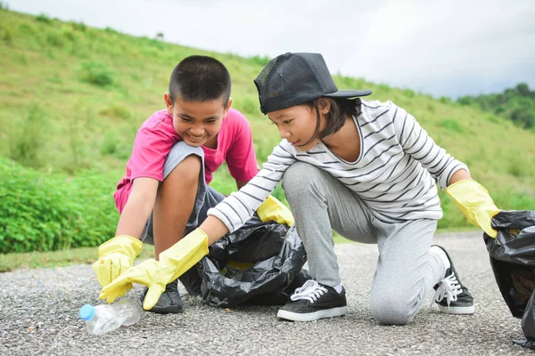 Las manos de los niños en guantes amarillos recogiendo vacío de botella de plástico —  Fotos de Stock