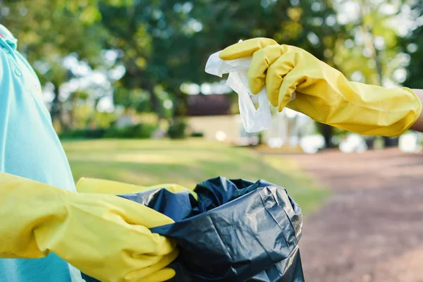 Ręce w rękawice żółty, zbierając puste butelki plastikowe do worka bin — Zdjęcie stockowe