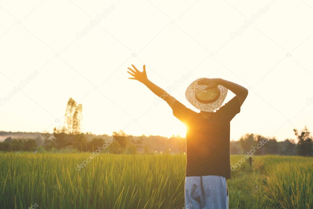 Happy boy open hand on green rice field during sunset