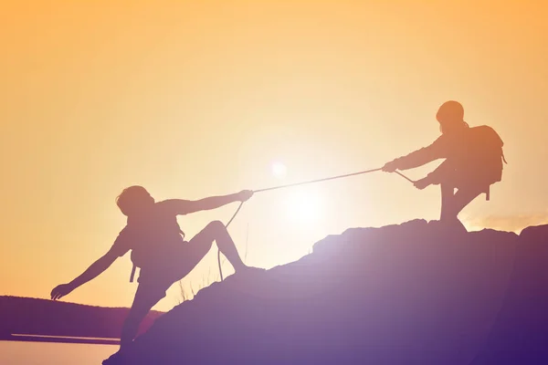 Silhouette di ragazza aiutare l'uomo lavoro di squadra di successo in cima alla montagna — Foto Stock