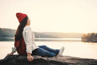Doğada kayaya oturan günbatımı, tatil kavramı seyahat, seçici ve yumuşak odak, yenilikçi stili rengini Relax zamanında sırasında mutlu Asyalı kadın