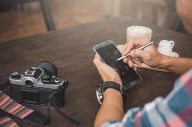 Mutlu genç adam kafe dükkanda smartphone kullanarak sakin tatil, hippi tarzı seçici ve yumuşak odak rengini zamanında