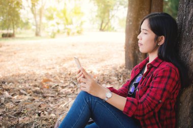 Büyük ağacın altında park üzerinde oturan smartphone kullanan an kadın zevk, tatil kavramı, vintage rengini zamanında sakin ol