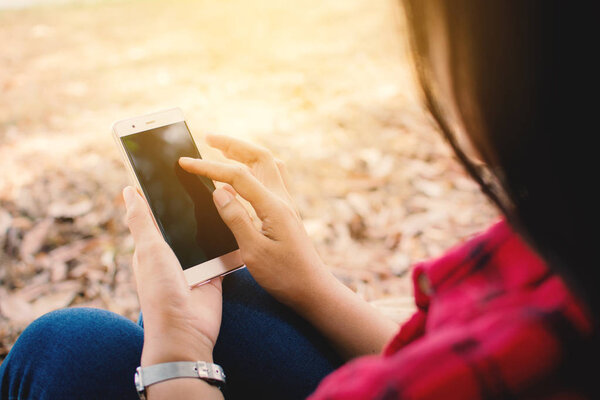 Enjoying moment woman using smartphone sitting under the big tree on park ,Relax time on holiday concept ,color of vintage