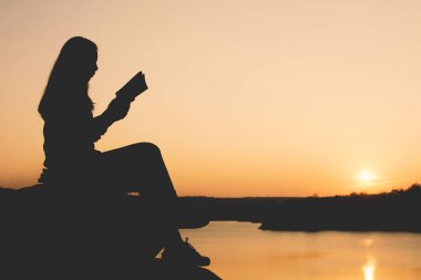 Siluet kadın günbatımı sırasında parkta bir kitap okuma