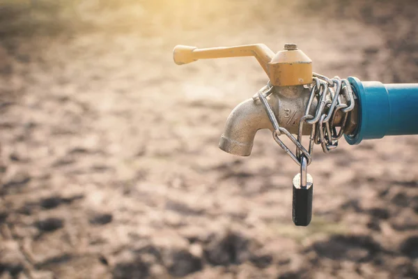 Key and chain locked faucet on cracked dry ground , concept drought and shortage of water