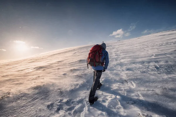 Człowiek alpinista wspina się na szczyt góry w zimie o świcie — Zdjęcie stockowe