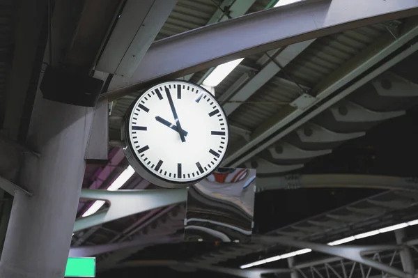 Белые простые часы, висящие на шесте на станции — стоковое фото