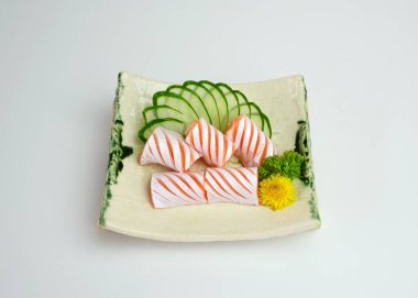 Dilimlenmiş çiğ somon kesesi sashimi ve tabakta salatalık.