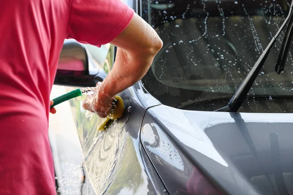 Worker washing and rubbing car with sponge and water