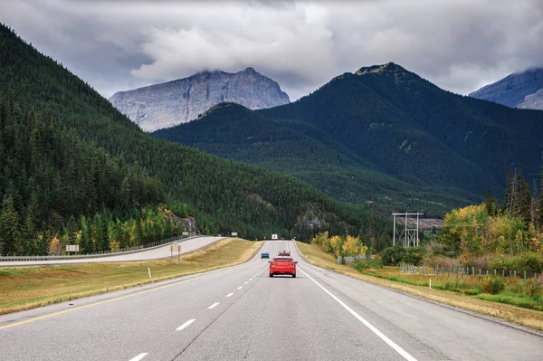 Voiture rouge conduite sur l'autoroute avec des montagnes rocheuses dans le parc national — Photo