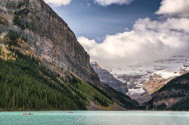 Turistler turkuaz gölde kano yapıyorlar ve Kanada Alberta 'da Louise Gölü' nde kayalık dağlar var.