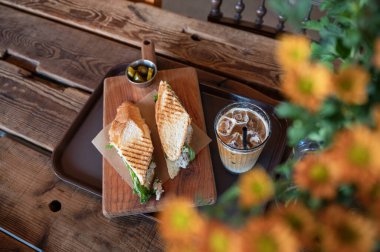 Buzlu kahve ve ahşap masada çiçek süslemeli tavuklu sandviç.
