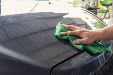 Arabanın kaputunda yeşil mikrofiber bez olan bir adam temizlik yapıyor.