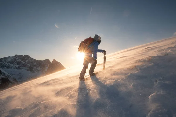 三脚を持つ男の写真家は 日没時に吹雪の中で立天山の斜面の丘に登っています — ストック写真