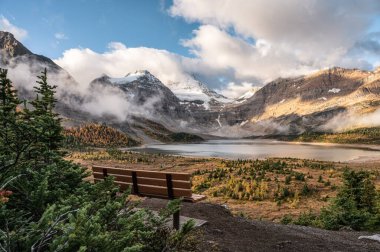 Wooden bench with mount Assiniboine and lake Magog in provincial park at British Columbia, Canada clipart
