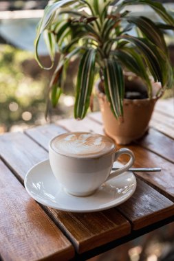 Köpük çiçekli sıcak latte ve kafedeki ahşap barda bitki süslemesi.