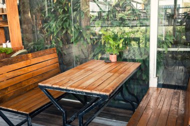 Ahşap yemek masası ve yemyeşil bitkilerle süslenmiş bank. 