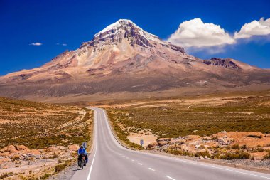 Cycling on the beautiful road in front of Nevado Sajama volcano clipart