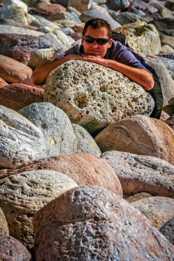 Sahilde büyük kayalar üzerine oturan adam