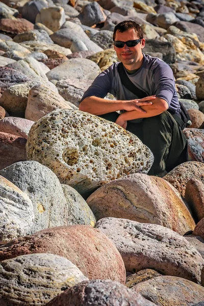 Sahilde büyük kayalar üzerine oturan adam