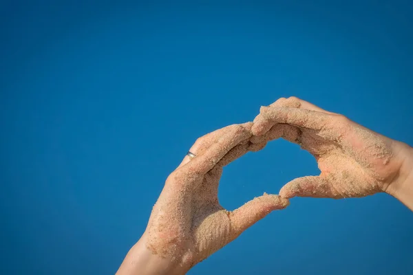 Ruce v písku pláže takže tvar srdce — Stock fotografie