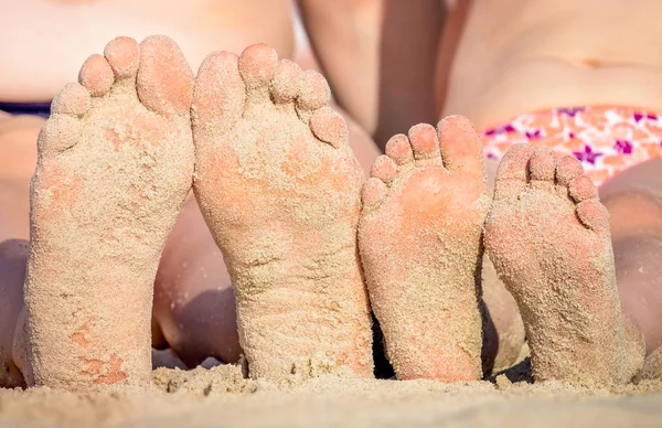 Mother and daughter feet covered in beach sand