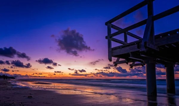 Sunset over wooden pier on the sea beach — Stock Photo, Image