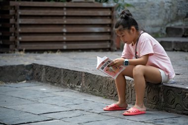 Küçük Çinli kız kitap okuyor.