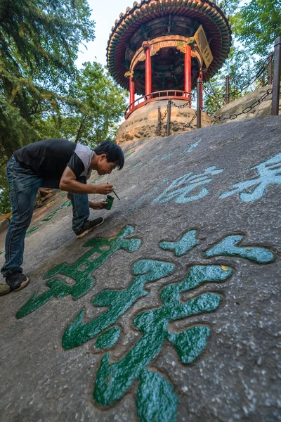 Uomo pittura cinese caratteri calligrafia su una roccia — Foto Stock