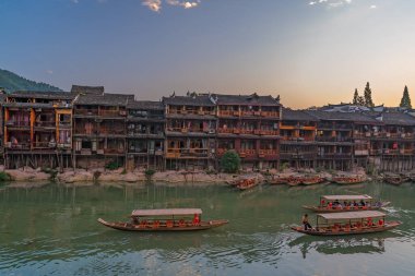 Feng Huang, Çin - Ağustos 2019: Eski tarihi ahşap turist tekneleri Tuo nehrinde yelken açarak Fenghuang Eski Kasabası 'nın merkezinden geçiyor.