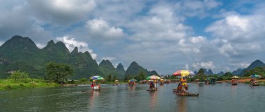 Yangshuo, Çin - Ağustos 2019: Manzaralı ve güzel Yulong Nehri üzerinde uzun çubuklarla rehberlik eden bambu sallarda oturan turistler