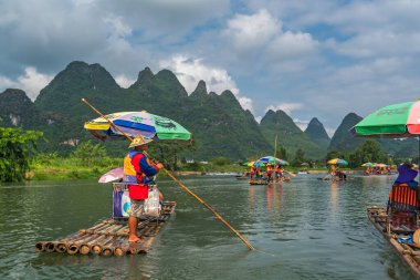 Yangshuo, Çin - Ağustos 2019: Manzaralı ve güzel Yulong Nehri üzerinde uzun çubuklarla rehberlik eden bambu sallarda oturan turistler