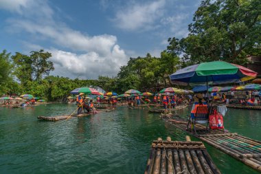Yangshuo, Çin - Ağustos 2019: Manzaralı ve güzel Yulong Nehri üzerinde uzun çubuklarla rehberlik eden bambu sallarda oturan turistler