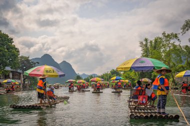 Yangshuo, Çin - Ağustos 2019: Manzaralı ve güzel Yulong Nehri üzerinde uzun çubuklarla rehberlik eden bambu sallarda oturan turistler