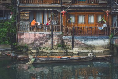 Feng Huang, Çin - Ağustos 2019: Eski tarihi batakhanelerinin balkonlarında oturan vatandaşlar, Tuo nehrinin kıyısındaki Diaojiao evleri, Fenghuang Eski Kasabası 'nın merkezinden akıyor.