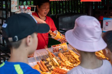 Chongqing, Çin - Ağustos 2019: Çinli kadın sokakta ahşap çubuklarda kızarmış et ve ızgara yiyecek satıyor.