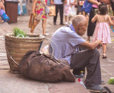 Chongqing, Çin - Ağustos 2019: Yaşlı yorgun Çinli adam kaldırımda büyük bir çanta ile dinleniyor