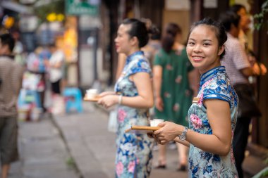 Chongqing, Çin - Ağustos 2019: Chongqing 'deki Ci Qi Kou antik kasabasının önünde duran güzel Çinli kadın ve insanların tatmaları için içecek çayı örnekleri dağıtıyor.
