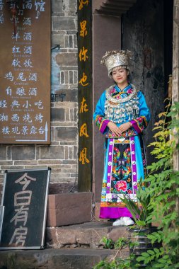 Feng Huang, Çin - Ağustos 2019: Geleneksel halk kostümü giymiş güzel Çinli kadın ve Hunan Eyaleti 'nin Fenghuang kentindeki eski binanın girişinin önünde poz veriyor.